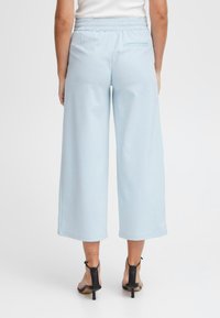 Lichtblauwe, brede broek met een elastische tailleband en een enkele achterzak, gemaakt van een gladde stof, gecombineerd met zwarte hoge hakken.