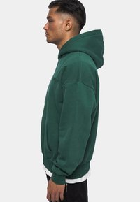 Groene, oversized hoodie met een voorzak, verstelbare trekkoordcapuchon en ribgebreide manchetten. Bevat een subtiele logo op de borst.