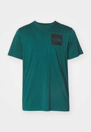 T-shirt di cotone teal con maniche corte, colletto tondo e una tasca quadrata nera con logo sulla parte sinistra del petto. Texture liscia.