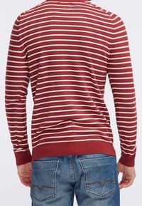 Pullover a righe rosse con strisce bianche. Polsini e orlo a costine. Indossato con jeans blu con tasche posteriori con cuciture a contrasto.