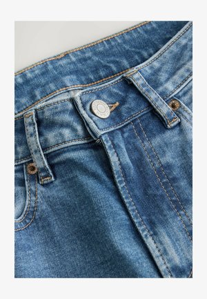 Blå denimjeans har et klassisk design med fem lommer, lukket med en metalknap og synlige syninger. Stoffet viser let falmning.