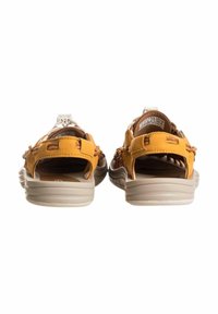 Sandales en daim jaune avec une sangle arrière et des accents marron, dotées d'une semelle texturée et d'un design ouvert pour la ventilation.