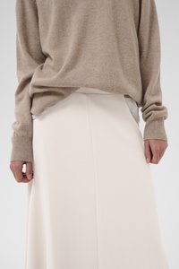 Beež kootud kampsun soonikkoes varrukasääreosadega, millele on lisatud lihtne elevandiluu värvi midi-seelik. Rõhk on pehmetel tekstuuridel ja lihtsal elegantsil riietuses.