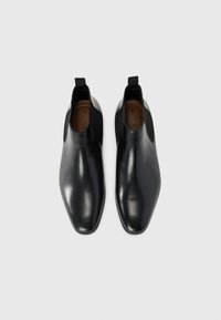 Botas Chelsea de cuero en negro, con una puntera redondeada elegante, paneles laterales elásticos y tiradores para facilitar el uso. Textura suave.