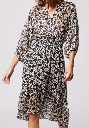 Robe à imprimé floral noir et blanc en tissu transparent, avec un décolleté en V, de longues manches bouffantes, et une taille smockée avec un ourlet volanté.