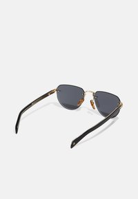 Ochelari de soare tip cat-eye cu lentile întunecate, cadru din metal auriu și brațe din acetat negru cu un model subtil. Pernele pentru nas transparente îmbunătățesc confortul.