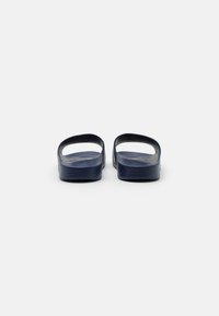 Mørkeblå slip-on sandaler med glatte teksturerte stropper og et åpent bakdesign, som har en flat såle for komfort.