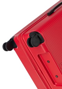 Valigia rigida rossa con texture a righe, ruote nere e chiusura a zip, che mette in evidenza il suo design elegante e il materiale resistente.