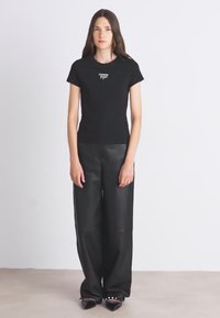 Μαύρο στενό μπλουζάκι με λεπτομέρεια λογότυπου, συνδυασμένο με παντελόνι μαύρης faux δερμάτινης φαρδιάς γραμμής. Το σύνολο ολοκληρώνεται με μαύρες μυτερές γόβες.