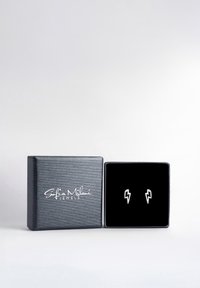 Silver blixtörhängen utställda i en svart sammetfodrad box med en texturerad svart exteriör som har vit varumärkestext.