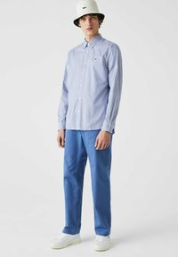 Camisa de botones a rayas azul y blanca, combinada con pantalones celestes y zapatillas blancas. Un sombrero tipo bucket blanco con un acento de logo negro.