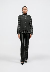 Γκρι πλεκτό γιλέκο πάνω από μαύρο και λευκό καρό πουκάμισο, συνδυασμένο με εφαρμοστές μαύρες δερμάτινες παντελόνες και τακούνια με μυτερό δάχτυλο.