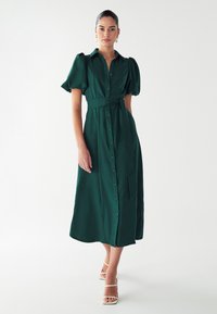 Zelena obleka do kolen s kratkimi gubastimi rokavi, gumbastim zapiranjem spredaj in pasom s pasom. Gladek material brez vzorcev.