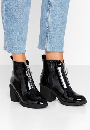 Ben iført lyseblå cropped jeans og skinnende sorte ankelstøvler med chunky hæle og forlynlås med cirkulært trækkefragment.