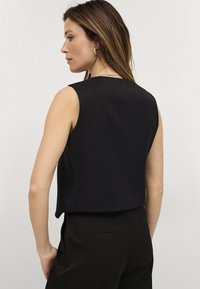 Zwarte mouwloze top met een gestructureerd ontwerp, gladde textuur en een cropped lengte, met een nette halslijn en minimale naaddetails.