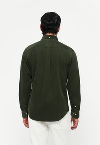 Donkergroene corduroy blouse met een button-down kraag, lange mouwen en een iets gebogen zoom, met subtiele textuur en stikdetails.