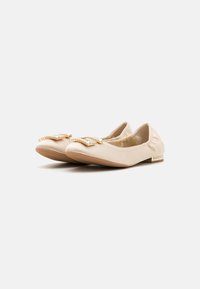 Ballerine beige con una texture liscia, caratterizzate da un fiocco con dettagli dorati e applicazioni di strass sulla punta, tacco basso e suola flessibile.