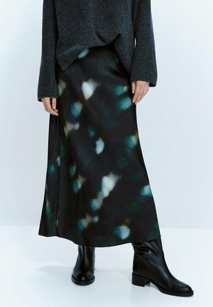 Woman wearing a dark gray sweater, black and teal abstract patterned skirt, and black mid-calf leather boots standing against a plain background.