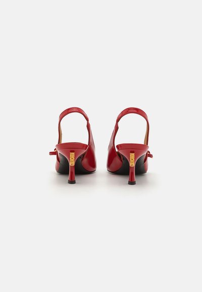Punane patentnahast slingback kontsaga jalanõud musta tallaga, terava varbaga ja õhukeste punaste kontsadega, millel on kuldne aktsent taga.