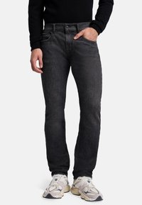 Schwarze Denim-Jeans mit geradem Schnitt, leichter Ausbleichung, minimalem Hardware-Einsatz und fünf Taschen, kombiniert mit hellen Sportschuhen.
