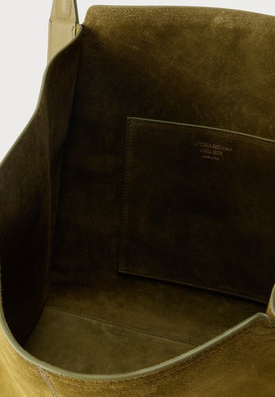 Εσωτερικό τσάντας από ανοιχτό καφέ καστόρι με ανοιχτή θήκη που έχει ανάγλυφο το όνομα της μάρκας στο εσωτερικό.