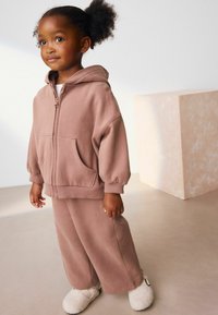 Un hoodie oversize rose clair avec une poche avant et des manches côtelées, associé à un pantalon large assorti et des chaussons crémeux et duveteux.