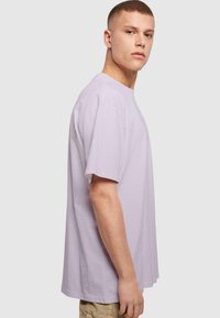 Lyslilla bomulds t-shirt med korte ærmer, afslappet pasform, rund hals og glat tekstur, vist på en model fra en sidevisning.