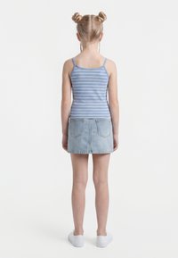 Chica con peinado de dos moños espaciales, vistiendo una camiseta sin mangas a rayas azules y blancas, falda de mezclilla y zapatillas blancas, de pie de espaldas.