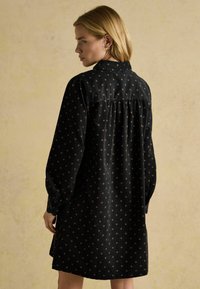 Melnā kleita ar garām piedurknēm un apkakli, ar mazu zvaigžņu motīvu zeltā. Plīšošanās aizmugurē pievieno struktūru. Mīksts audums.
