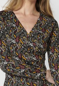 Czarna sukienka z tkaniny w kwiatowy wzór w kolorach żółtym, różowym, czerwonym i białym. Posiada dekolt w serek i długie rękawy z krojem kopertowym.