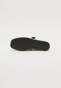 Semelle en caoutchouc noir avec une texture antidérapante, dotée d'un bord en jute naturel. Design plat, adapté pour un usage décontracté, avec peu d'ornements.