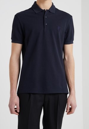 Polo blu navy con collo classico, patta con tre bottoni e piccolo logo ricamato sul petto. Maniche corte con tessuto strutturato.