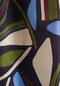 Tessuto astratto con uno sfondo scuro e grandi forme in verde, azzurro, beige e rosso, che presenta una texture liscia e un motivo vivace.