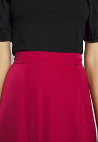 Strakke zwarte top met pofmouwen, gecombineerd met een knielange, felroze rok met een gladde textuur en een platte tailleband.