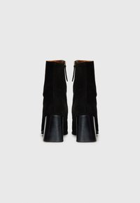 Bottines en daim noir avec une texture lisse, dotées d'une fermeture éclair et d'un talon noir épais et effilé.