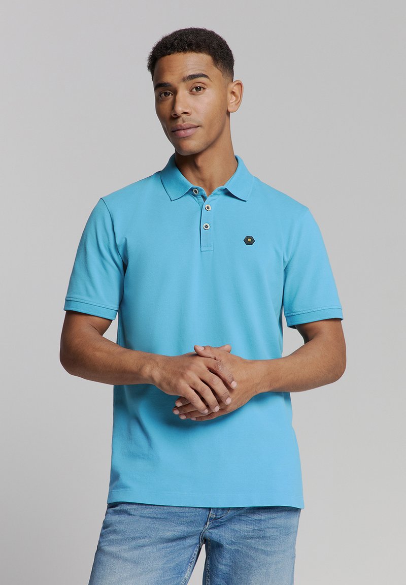 Katoenen polo shirt in levendig blauw met een kraag, een placket met twee knopen en een klein zwart hexagonaal logo op de linkerborst. Korte mouwen.
