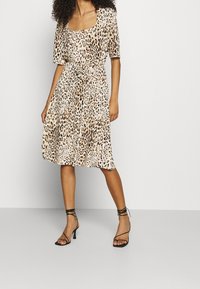 Leopardmönstrad klänning i mjukt tyg, med fyrkantig halsringning, korta ärmar och en utsvängd kjol med knyt i midjan. Svarta remsandaler.