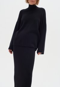 Zwart gebreid twee-delig outfit met een lange mouwen turtleneck trui en een aansluitende rok, beide met een zachte textuur en een minimaal ontwerp.