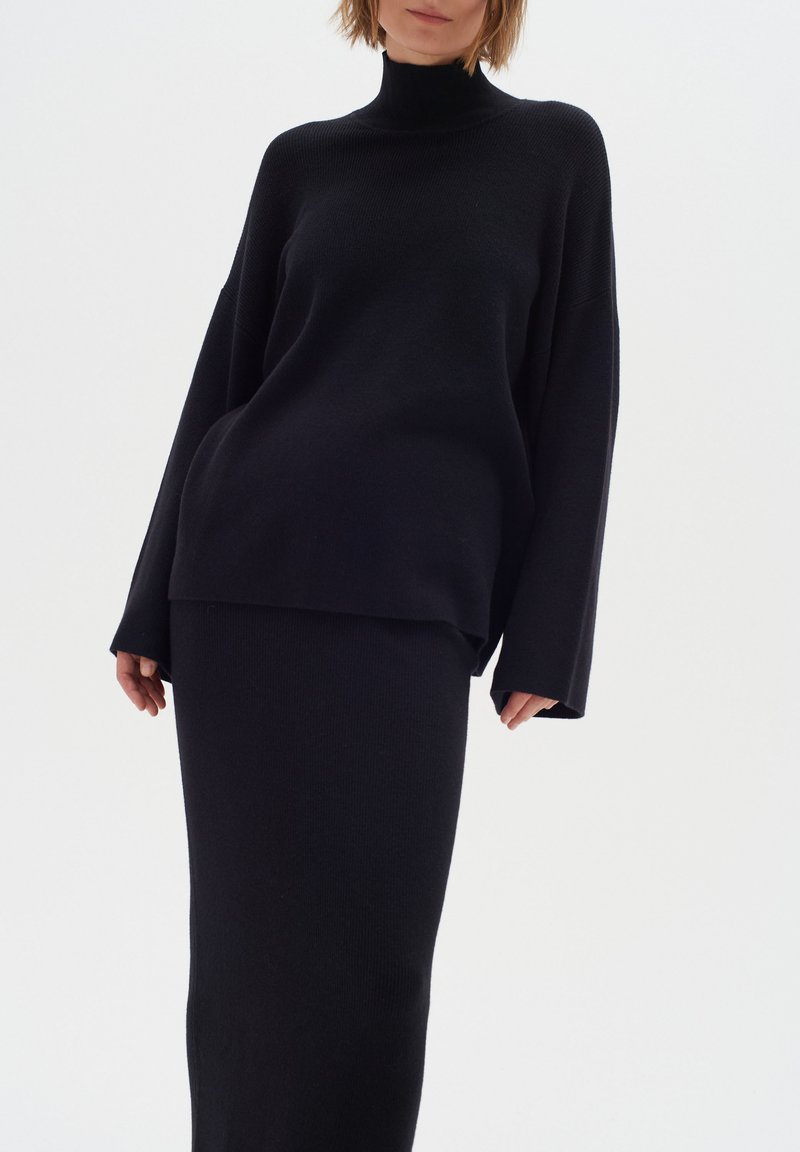 Zwart gebreid twee-delig outfit met een lange mouwen turtleneck trui en een aansluitende rok, beide met een zachte textuur en een minimaal ontwerp.