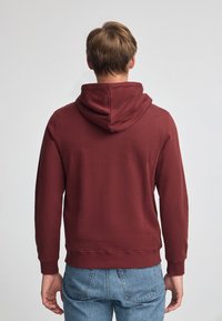 Felpa con cappuccio bordeaux, in tessuto misto cotone, vestibilità rilassata, polsini e orlo a costine, vista posteriore che mostra il cappuccio e un design semplice senza grafiche.