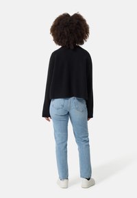 Pull noir court avec texture côtelée, associé à un jean droit bleu clair et des baskets blanches, vu de dos.