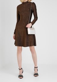 Abito marrone scintillante a maniche lunghe con corpetto aderente e gonna svasata. Abbinato a sandali neri con tacco e borsa a tracolla argentata.