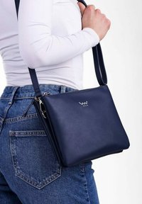 Námořnická kožená crossbody taška s obdélníkovým tvarem, elegantním designem, zipovým uzávěrem a stříbrným logem. Součástí je nastavitelný popruh.