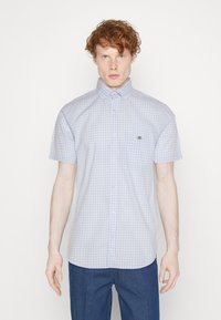 Chemise à manches courtes, à carreaux bleu et blanc, avec un col boutonné, dotée d'une poche poitrine et d'un logo subtil.