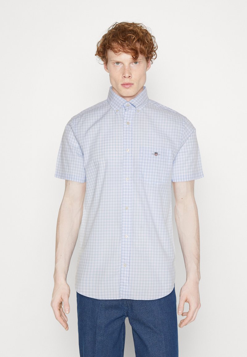 Chemise à manches courtes, à carreaux bleu et blanc, avec un col boutonné, dotée d'une poche poitrine et d'un logo subtil.