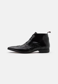 Botas de tobillo de cuero negro con punta afilada, con acentos de textura de cocodrilo y detalles de brogue decorativos. Cintas delgadas y lengüeta de agarre.