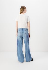 Jeans de corte ancho en azul claro, con un lavado deslucido, cinturilla elástica y bolsillos traseros. Combinados con una camiseta blanca básica.