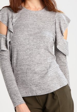 Gray long-sleeve top with ruffled shoulder cut-outs, textured knit fabric, fitted design, and round neckline. Paired with brown pants.