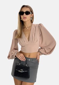 Rosa, kurz geschnittene Bluse mit gefältetem Design und voluminösen Ärmeln, kombiniert mit einem grauen Minirock und einer kleinen schwarzen, strukturierten Handtasche.