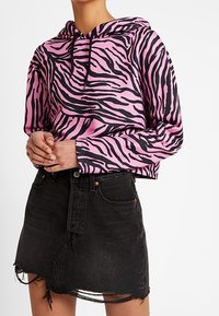 Persona che indossa una felpa con stampa zebra rosa e nera abbinata a una mini gonna di jeans nera con effetto usurato.